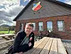 En mann sitter ved et piknikbord foran et klubbhus i murstein med Skade IL-logo på gavlen.