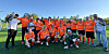 En gruppe fotballspillere og trenere poserer på en gressbane i solskinn.