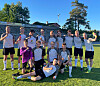 En gruppe fotballspillere poserer samlet på en gressbane i sollys etter kamp.