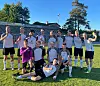 En gruppe fotballspillere poserer samlet på en gressbane i sollys etter kamp.